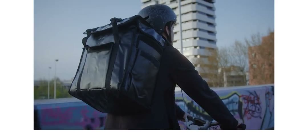 Un corriere in bicicletta in città, pacco sulle spalle